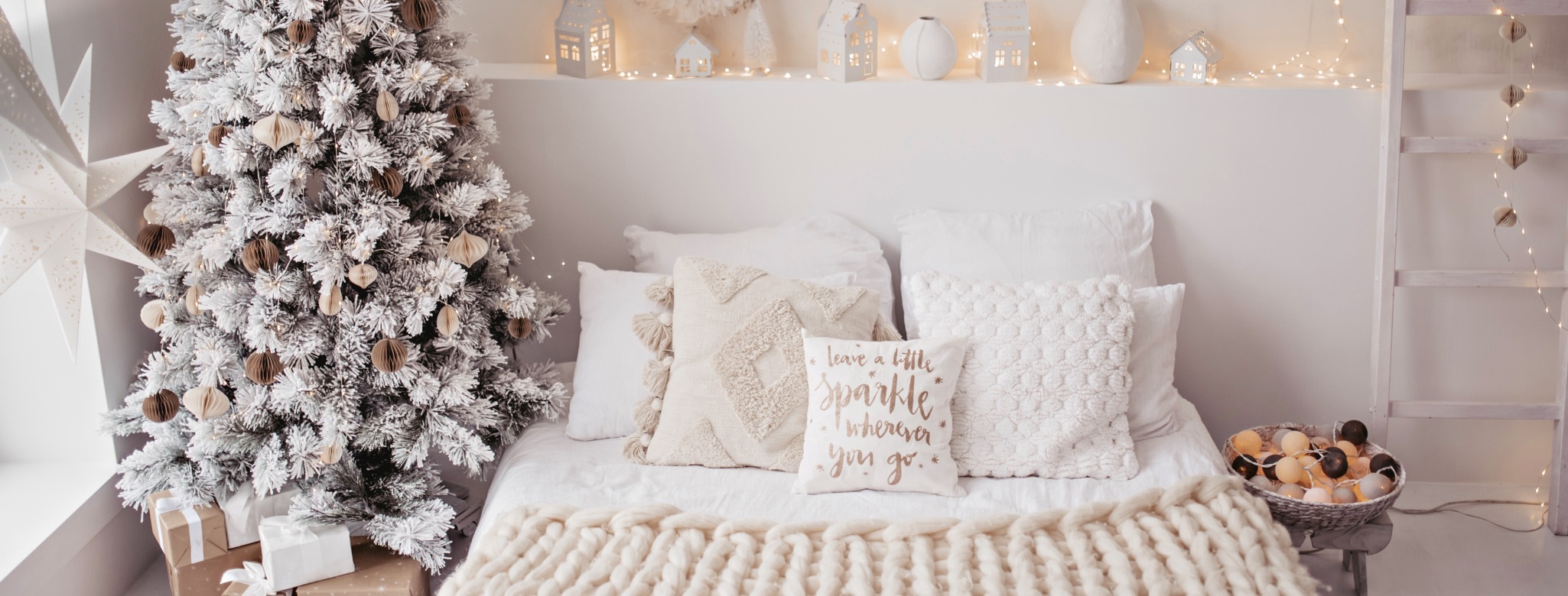 Photo of bedroom decorated with a christmas tree and layers of white and cream on the bed with festive pillows for holiday decorating tips
